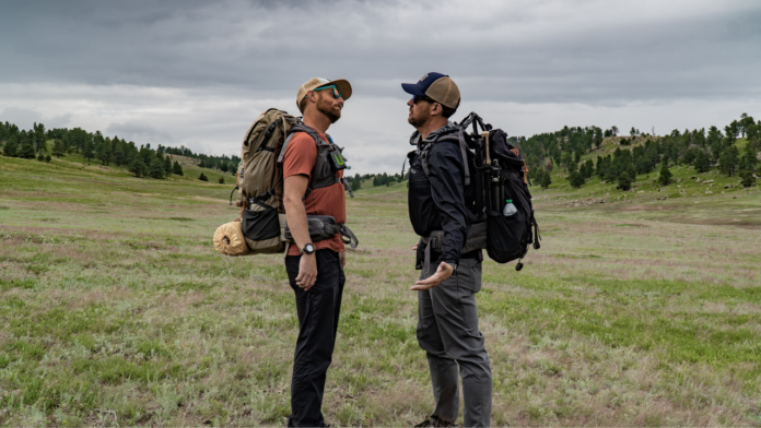 dan becker and eric hanson facing off in front of an open field while they compare their hiking and backpacking gear