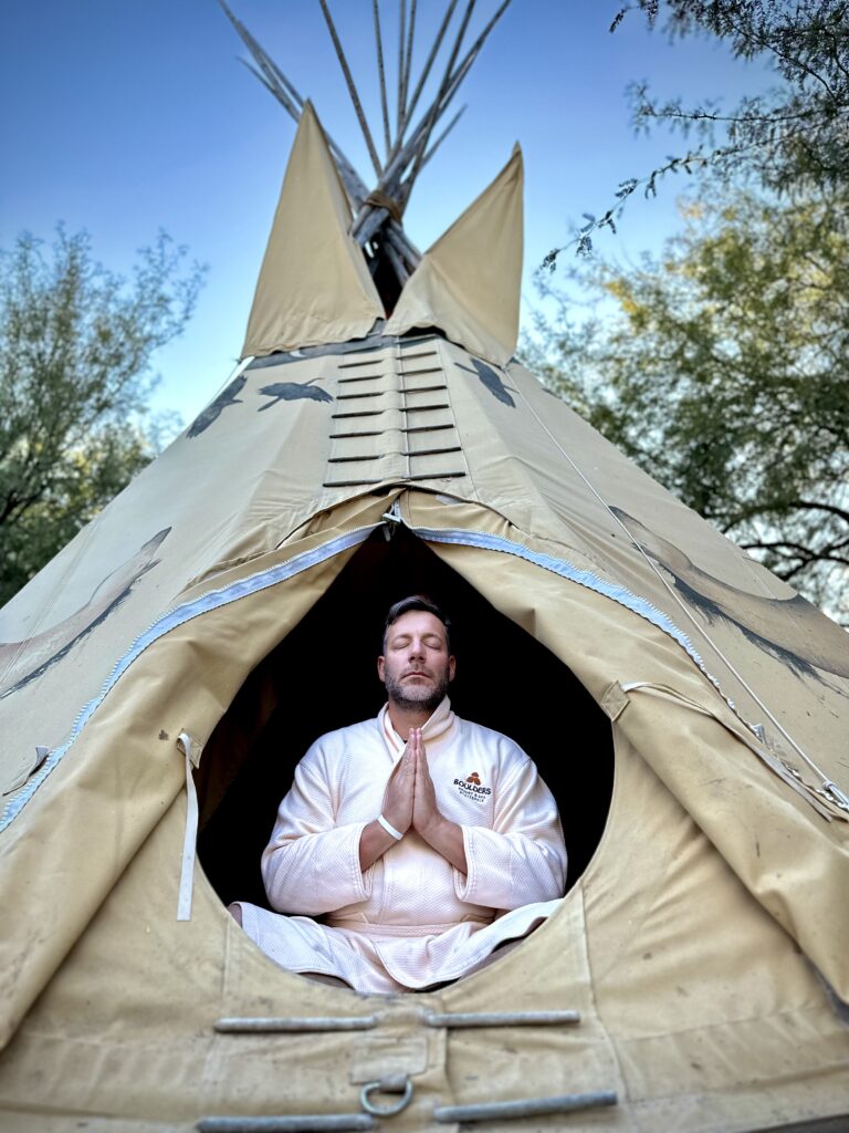 Jonathan Thompson sitting with hands in prayer in a teepee wearing a bathrobe, Scottsdale, Arizona