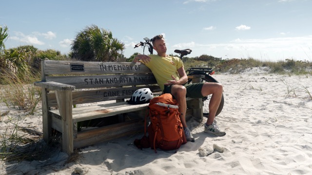 Host, Chef Corso, sitting on a bench on the beach on a sunny day.