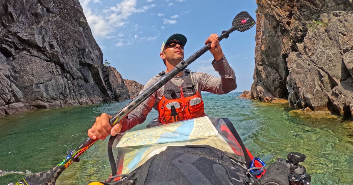 Ken Whiting in a kayak entering one of Lake Superior's dramatic sea caves, showcasing the region's unique natural features.