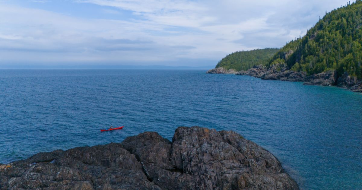 Ken Whiting paddling a kayak across the calm, clear waters of Lake Superior, surrounded by water and forests.